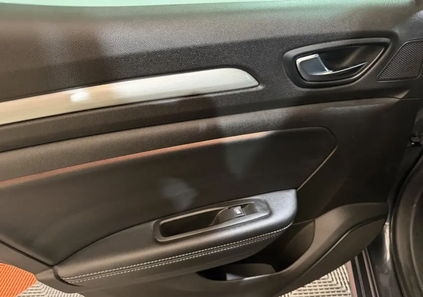 Gros plan sur la porte intérieure côté droit de la Renault Mégane Intens gris foncé, avec poignée et commande de lève-vitre.