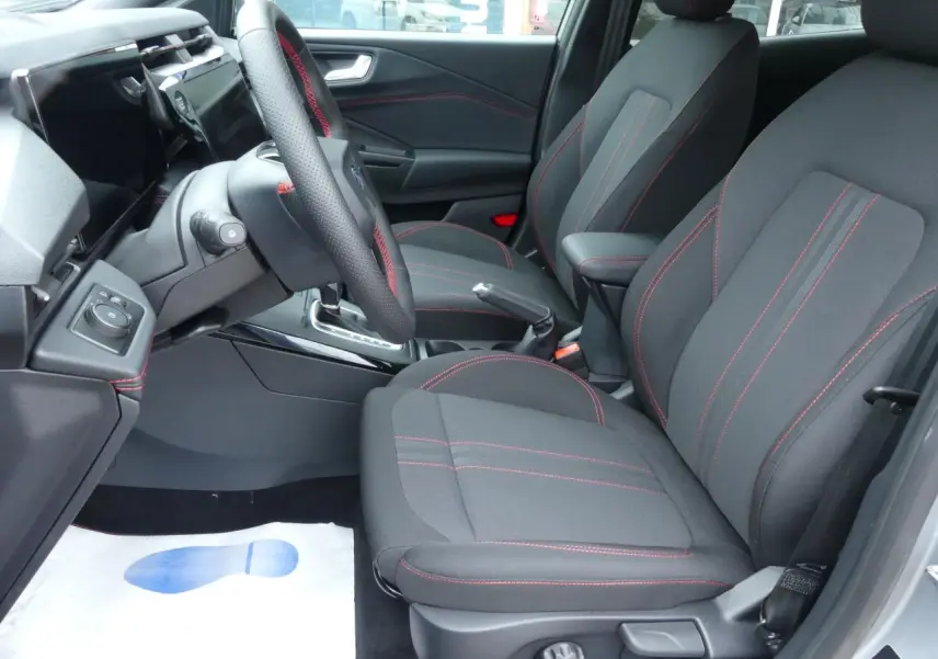 Vue intérieure côté conducteur du Ford Puma 2025, sièges noirs avec surpiqûres rouges et volant cuir perforé.