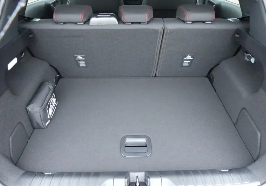 Vue du coffre spacieux et tapis noir du Ford Puma 2025 gris métallisé, avec sièges arrière rabattus et trousse de secours.
