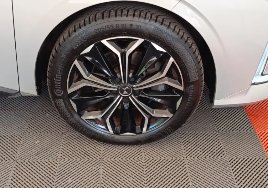 Gros plan sur la roue avant droite d'une DS4 E-TENSE 225 gris clair avec jante noire et argentée au design géométrique.