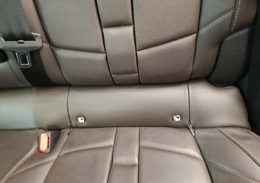Gros plan sur la banquette arrière en cuir marron perforé du DS4 E-TENSE 225 LA PREMIERE, avec ceintures visibles.