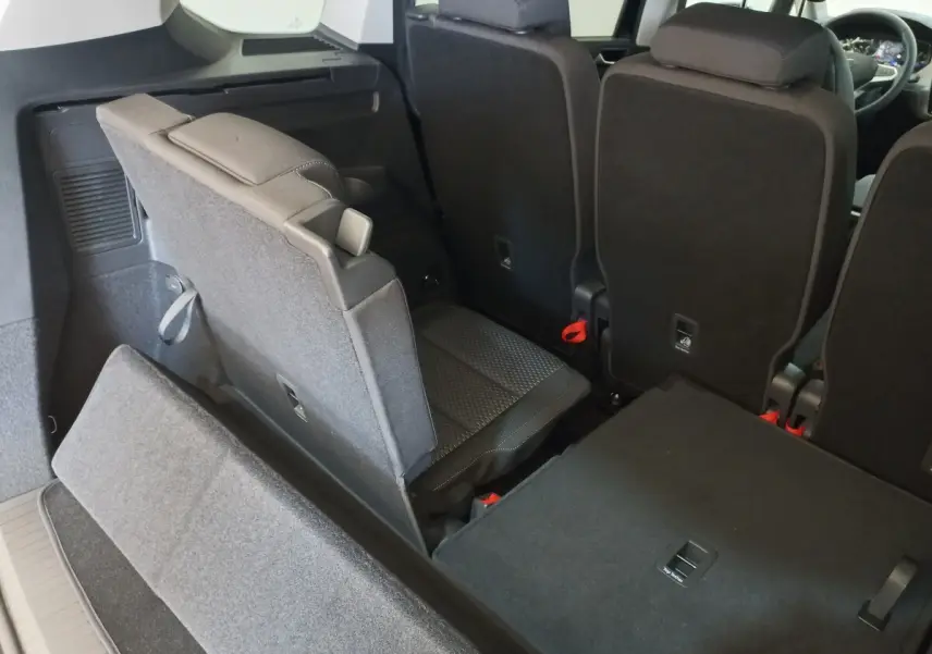 Vue intérieure arrière du Volkswagen Touran 2024 noir, montrant la troisième rangée de sièges partiellement relevée.