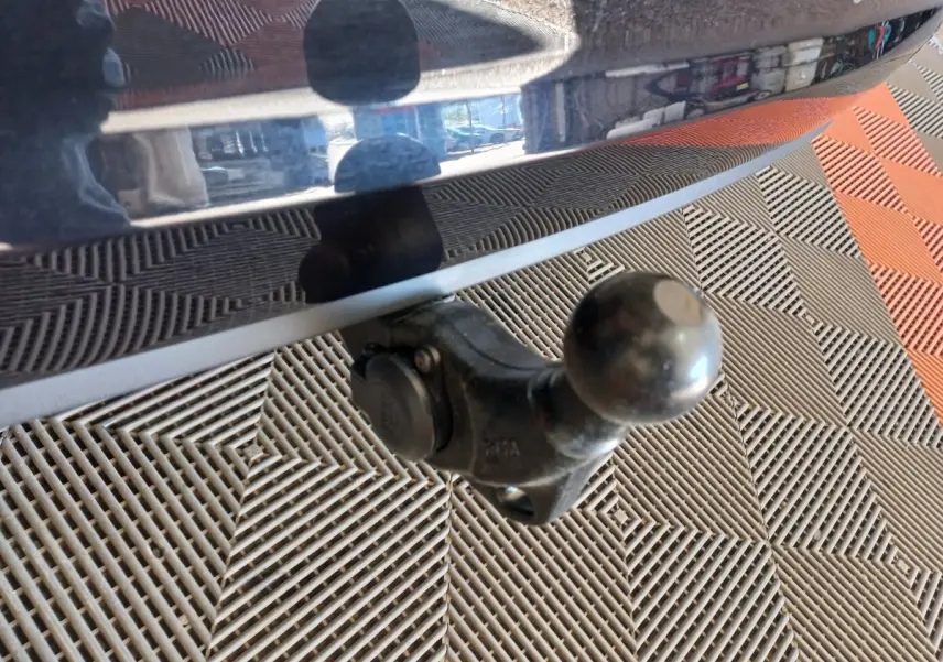 Gros plan sur l'attelage noir fixé à l'arrière d'un Volkswagen Touran noir, avec sol en damier gris et orange.