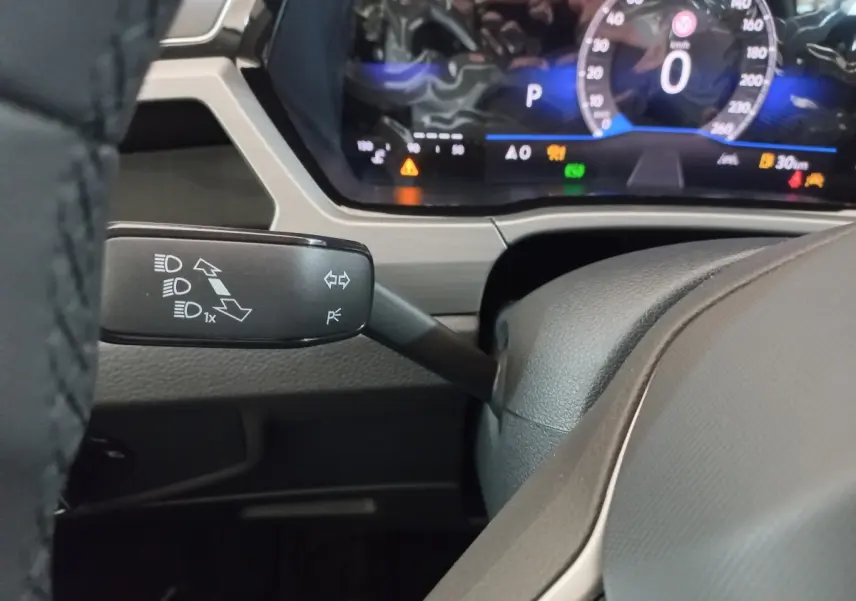 Gros plan sur la manette de clignotant gauche et le combiné d'instruments numérique du Volkswagen Touran 2024 noir.