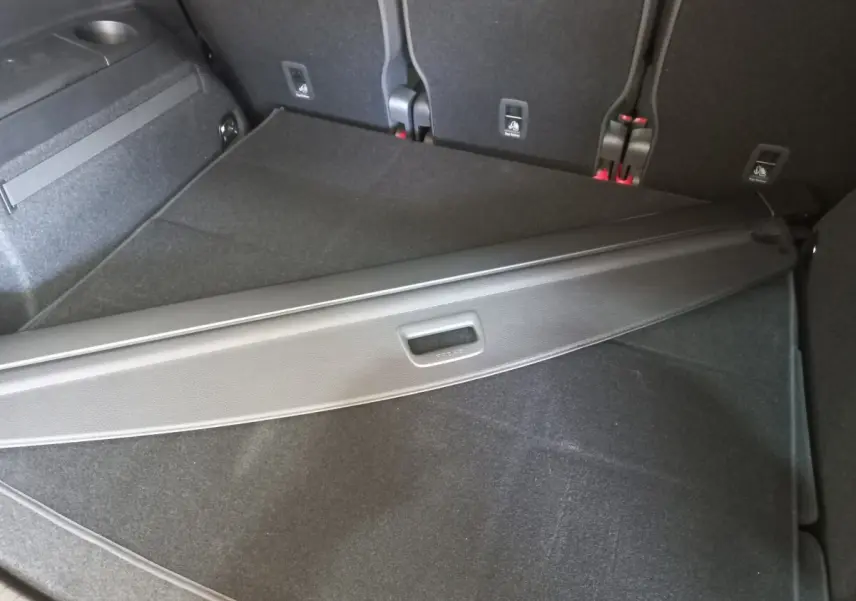 Coffre noir du Volkswagen Touran 2024 vu de dessus, avec cache-bagages partiellement déployé et sièges arrière rabattus.