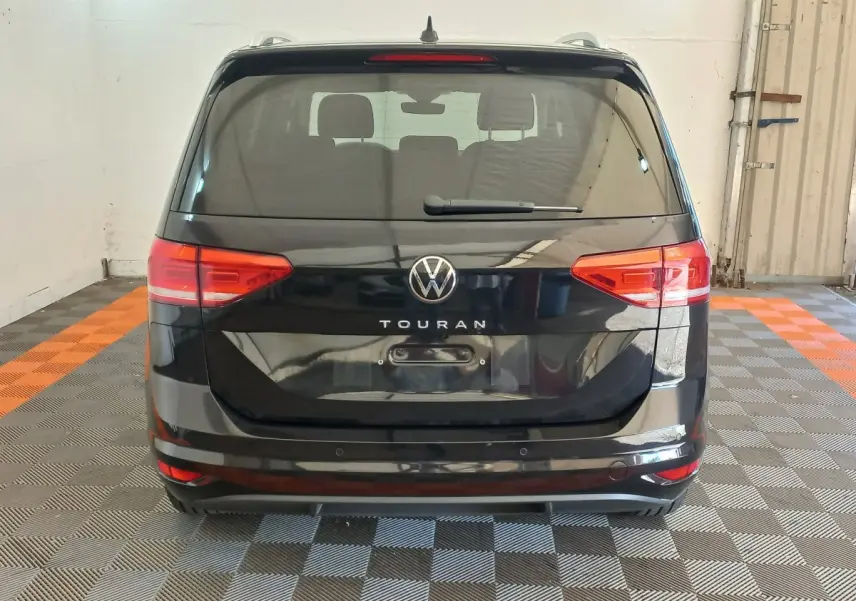 Vue arrière d’un Volkswagen Touran noir 2024 avec feux arrière rouges et logo central visible.