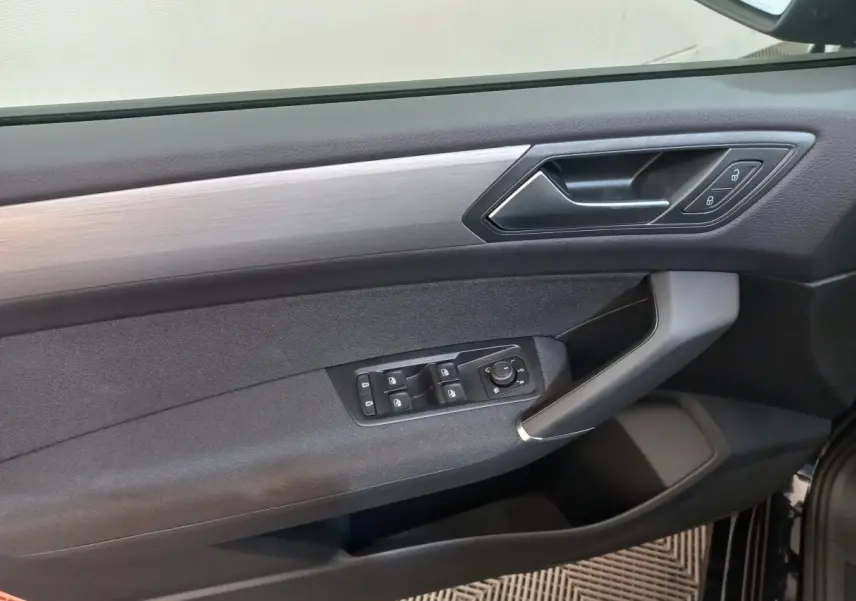 Détail de la porte avant gauche du Volkswagen Touran 2024 noir, avec commandes électriques et insert argenté.