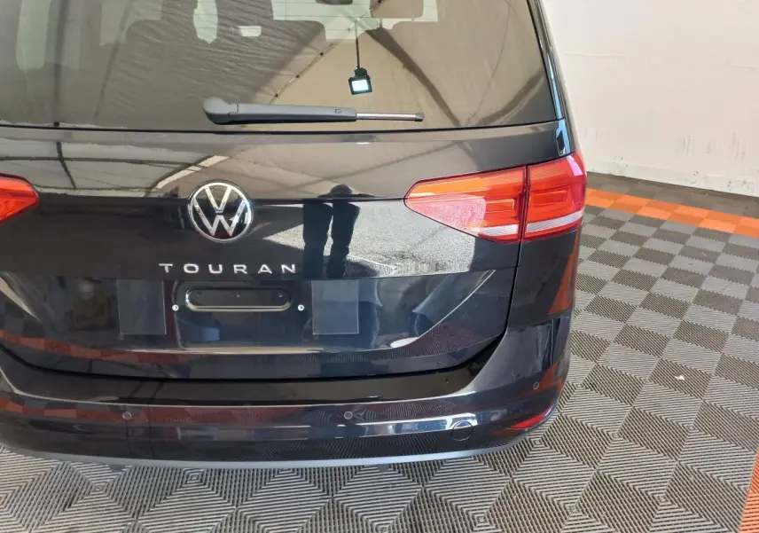 Vue arrière du Volkswagen Touran noir 2024 avec feux rouges et logo VW bien visibles sur fond de sol damier.