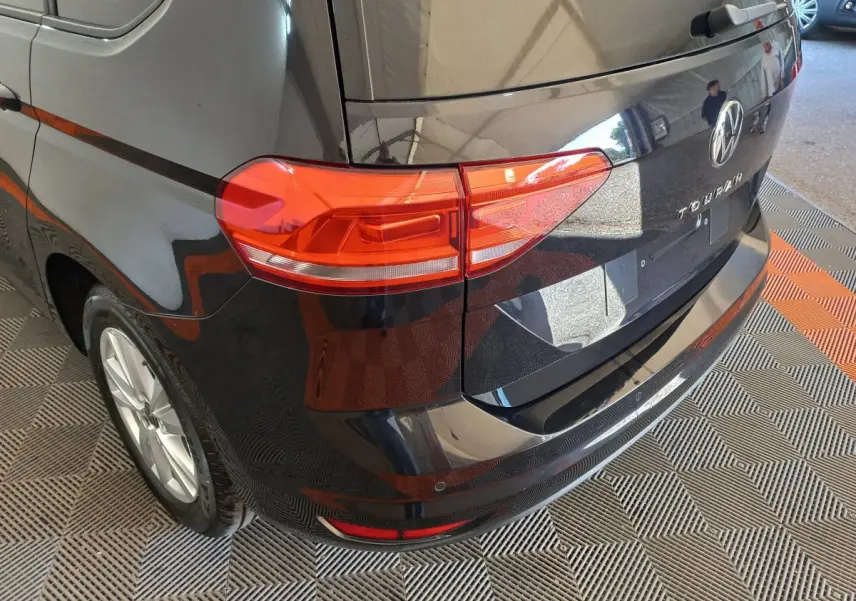 Vue 3/4 arrière droite d’un Volkswagen Touran noir 2024 avec feux arrière rouges et logo VW visible.