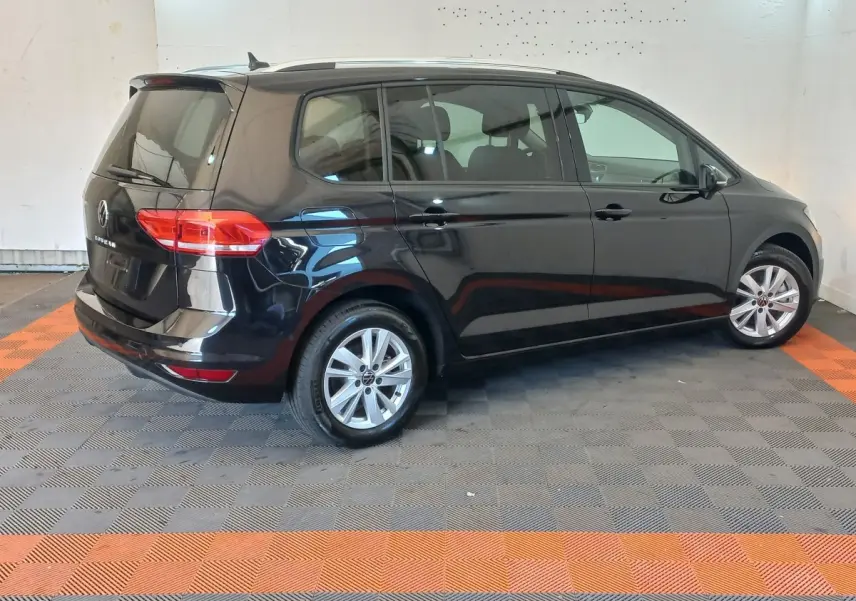 Volkswagen Touran noir vu de profil côté droit dans un intérieur avec sol gris et bandes orange.