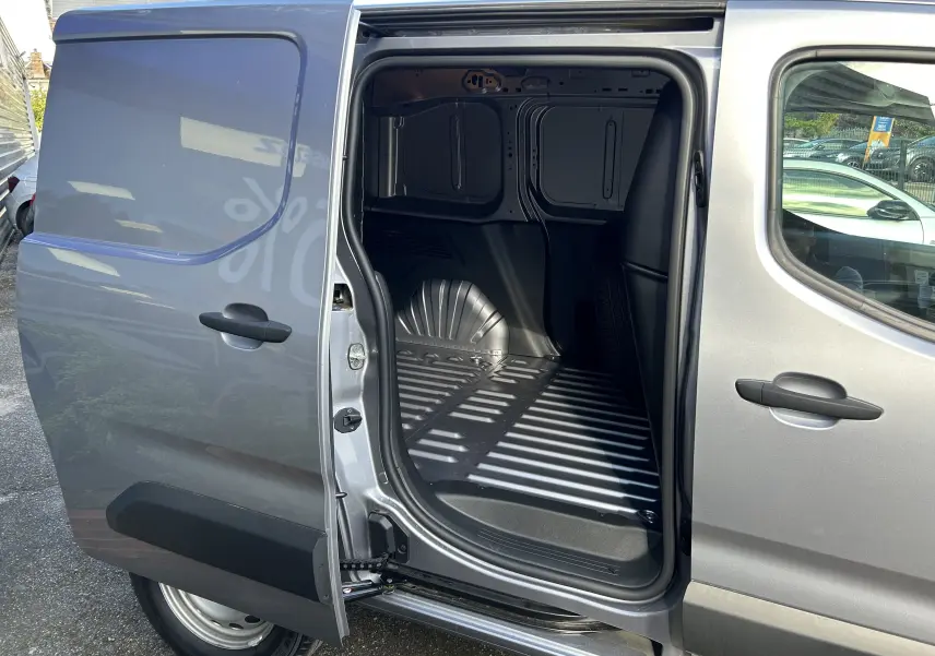 Vue latérale gauche du Peugeot Partner Dangel gris Artense avec porte coulissante ouverte dévoilant l’espace de chargement vide.