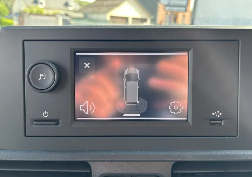 Écran tactile intérieur du DANGEL Partner 2025 affichant l'aide au stationnement avec vue du véhicule en gris Artense.