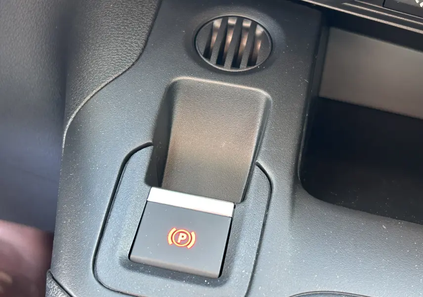 Gros plan sur le bouton de frein à main électrique rouge dans l'habitacle noir du DANGEL Partner gris Artense.