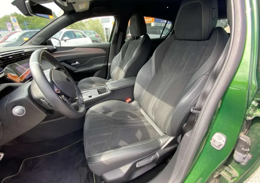 Vue intérieure côté conducteur de la Peugeot 308 2023 vert olivine, avec sièges en tissu et cuir noir et tableau de bord moderne.