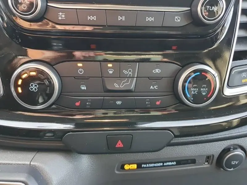 Vue rapprochée du tableau de bord noir du Ford Transit Custom blanc, montrant les commandes de climatisation et les voyants allumés.