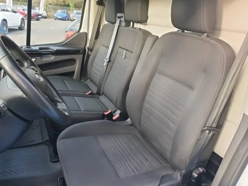Vue intérieure côté conducteur du Ford Transit Custom Fourgon 2020, sièges en tissu gris avec ceintures de sécurité visibles.