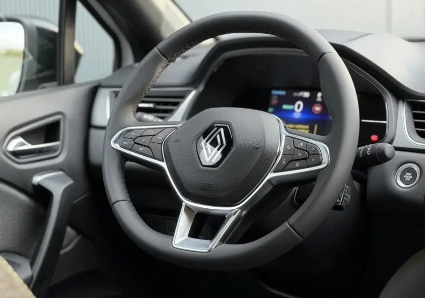 Vue rapprochée du volant noir et du tableau de bord numérique du Renault Captur blanc nacré 2025 en intérieur.