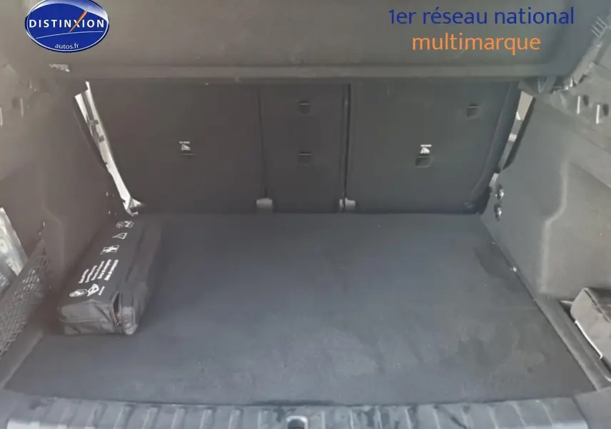 Coffre ouvert d’un BMW X1 blanc mineral, vue de l’arrière montrant un espace de chargement propre et un kit de sécurité noir.