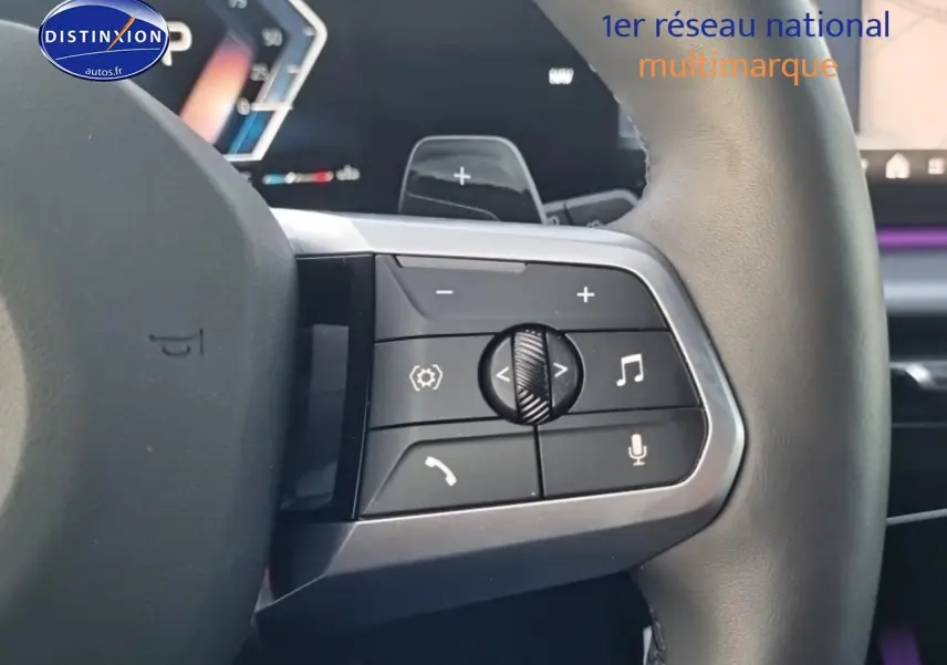 Gros plan sur les commandes multifonctions du volant cuir de la BMW X1 2025, avec éclairage d'ambiance violet en arrière-plan.