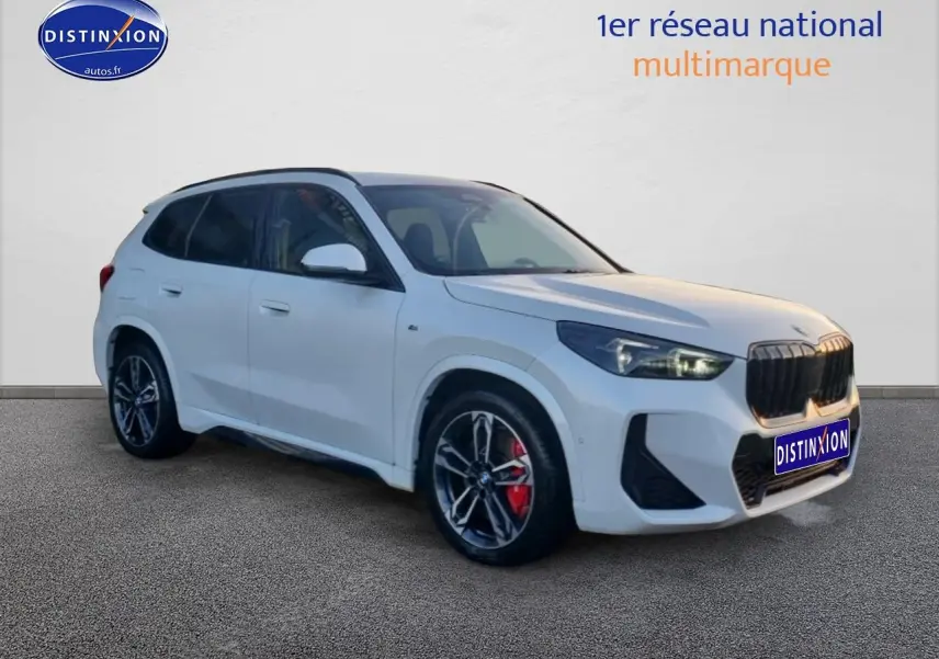 BMW X1 2025 blanc minéral en 3/4 avant droit, avec jantes alliage bicolores et étriers de frein rouges visibles.