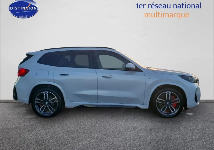 BMW X1 blanc minéral en vue de profil côté gauche, avec jantes alliage M bicolores et freins rouges visibles.