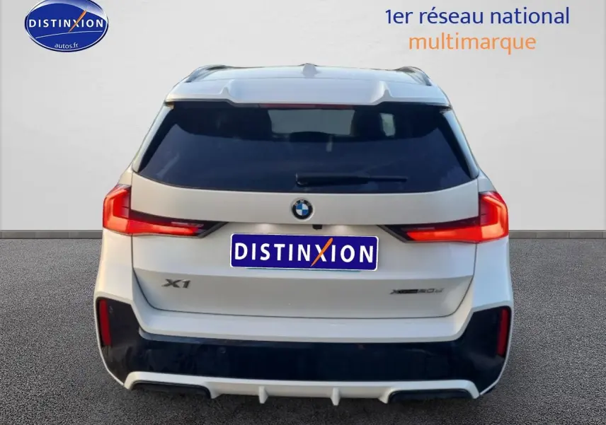 Vue arrière d’un BMW X1 blanc minéral avec feux LED et logo distinctif sur fond neutre.