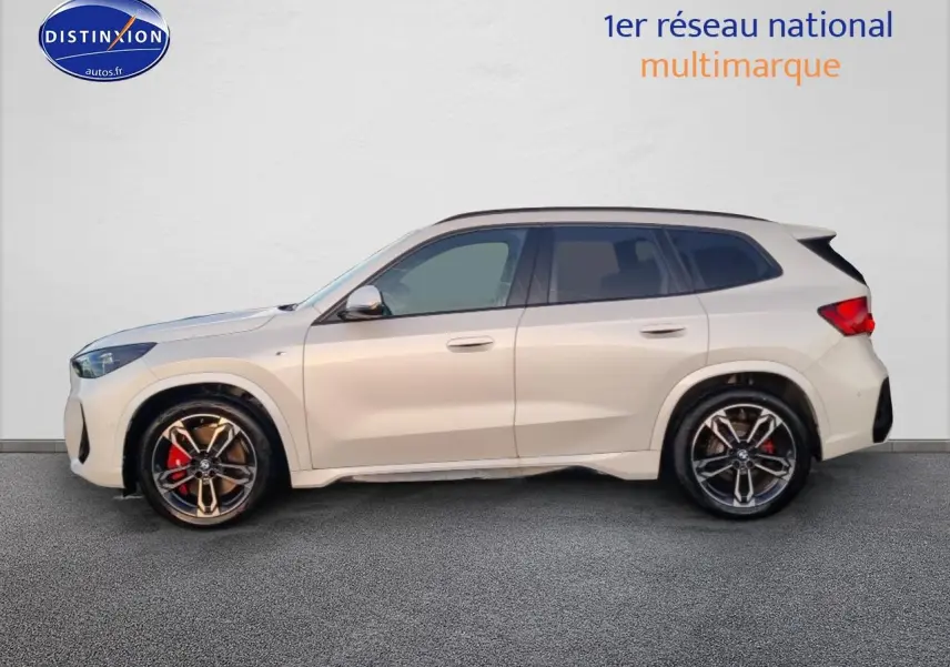 Profil gauche d’un BMW X1 blanc minéral avec jantes alliage bicolores et étriers de frein rouges.