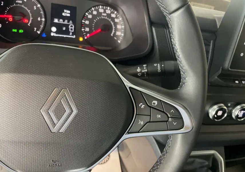 Vue rapprochée du volant noir de Renault Trafic Fourgon 2025 avec commandes intégrées et tableau de bord en arrière-plan.