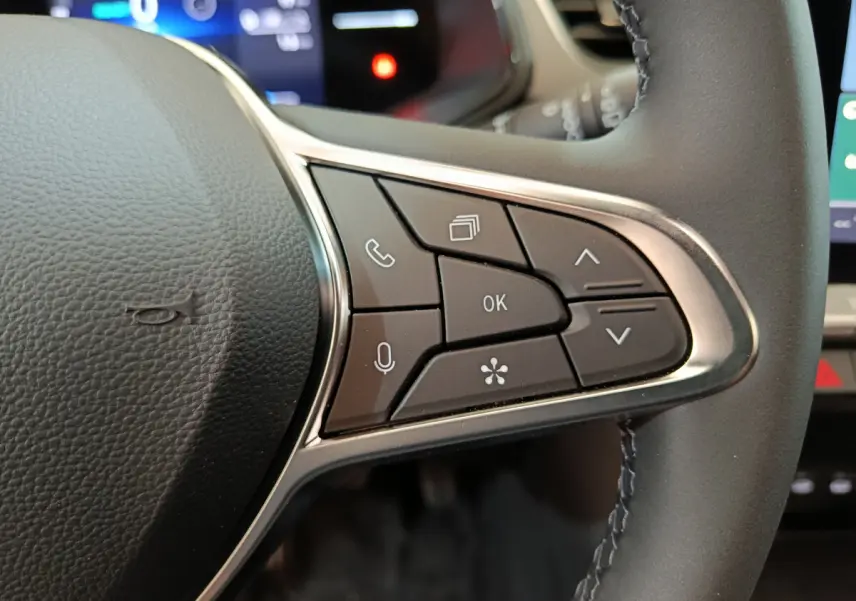 Gros plan sur les commandes multifonctions du volant cuir noir du Renault Captur blanc, version techno E-Tech 2025.