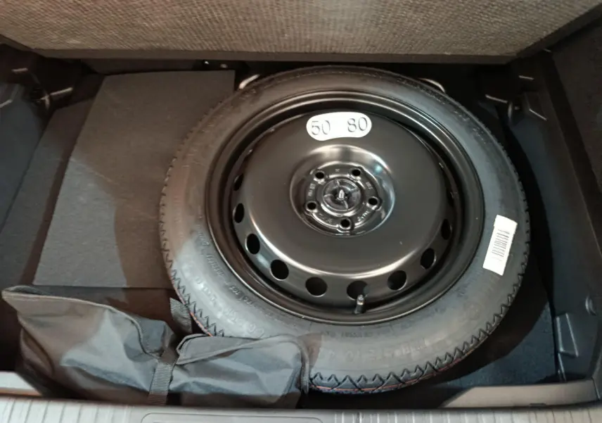 Roue de secours noire dans le coffre d'un Renault Captur blanc, vue en plongée sur le pneu galette et son rangement.