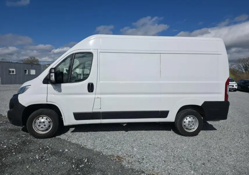 Vue latérale droite d’un fourgon Opel Movano blanc avec portes latérale coulissante et jantes tôles grises sur sol gravillonné.