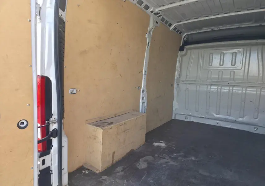Vue intérieure arrière du fourgon Opel Movano blanc, montrant l'espace de chargement avec parois en bois et sol noir.