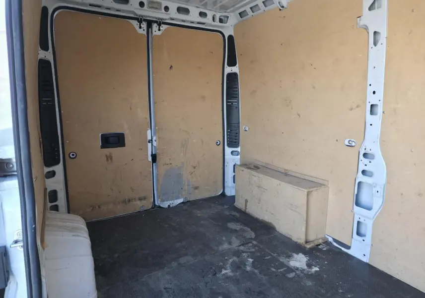 Vue intérieure arrière du fourgon Opel Movano blanc, montrant l'espace de chargement avec parois en bois et sol noir.