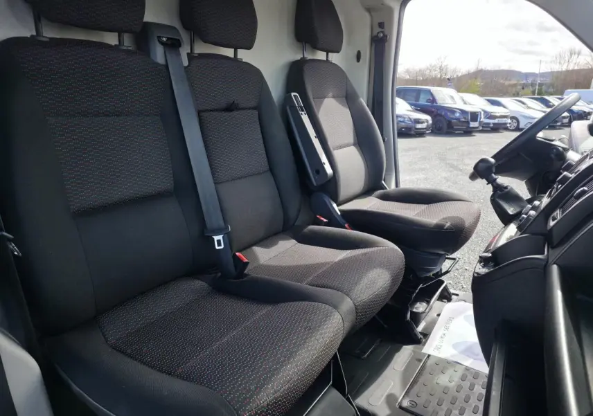 Vue intérieure côté conducteur de l’Opel Movano Fourgon 2022, sièges tissu noir avec motifs rouges et tableau de bord visible.