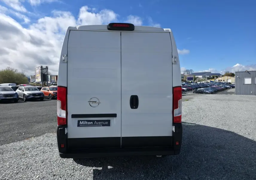Vue arrière d’un utilitaire Opel Movano blanc avec portes battantes et feux rouges verticaux sur un parking.