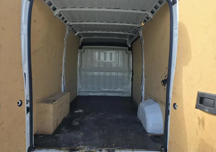 Vue intérieure arrière du fourgon blanc Opel Movano avec parois en bois et sol noir usé.