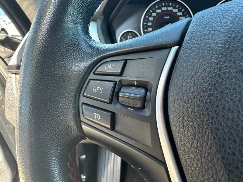 Gros plan sur les commandes du régulateur de vitesse au volant cuir noir de la BMW Série 4 Gran Coupe F36 418dA 2018.