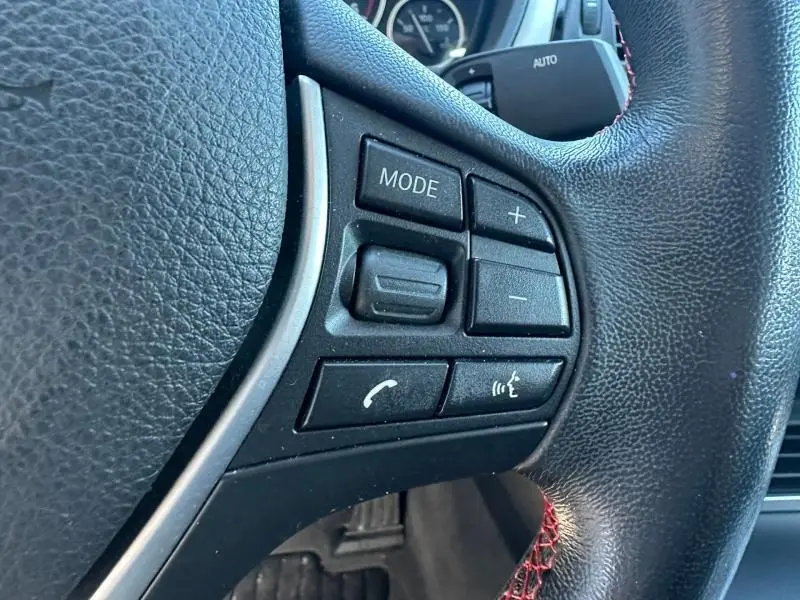 Gros plan sur les commandes multifonctions noires du volant cuir noir avec surpiqûres rouges d’une BMW Série 4 Gran Coupe F36 418dA Sport 2018.