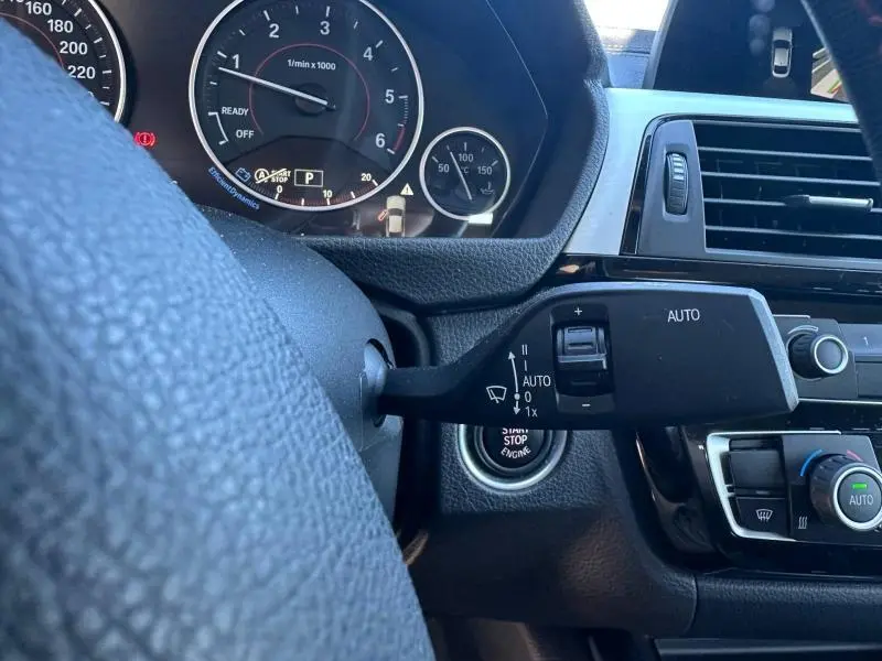 Gros plan sur le commodo d’essuie-glace à gauche du volant cuir d’une BMW Série 4 Gran Coupe noire, tableau de bord visible.