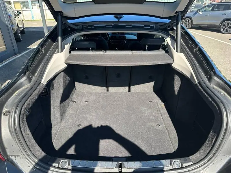 Coffre ouvert vu de l'arrière d'une BMW Série 4 Gran Coupe noire avec cache-bagages et intérieur en tissu gris.