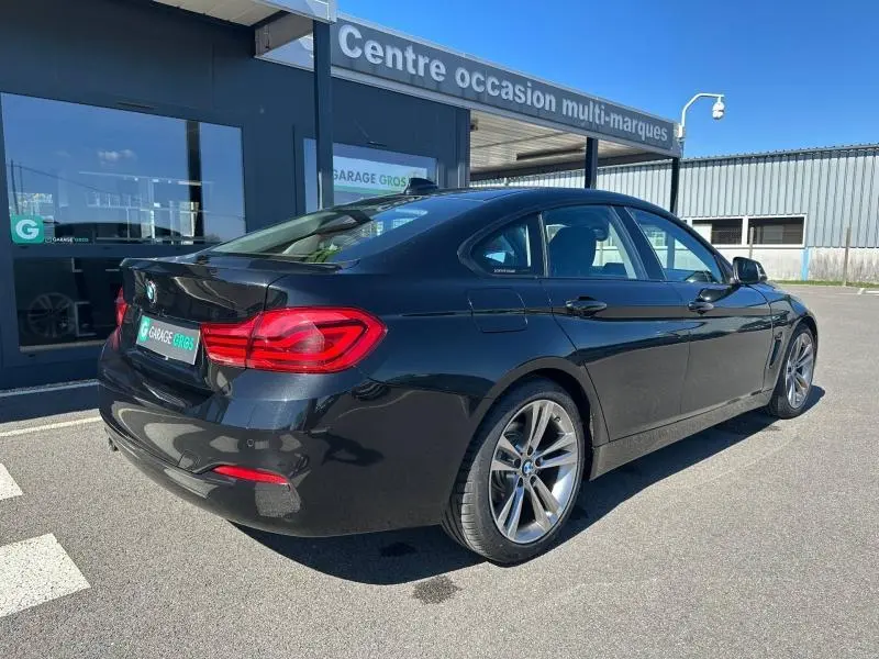 BMW Série 4 Gran Coupe noir vue 3/4 arrière droit, avec jantes alu et feux arrière LED visibles, stationnée devant un garage.
