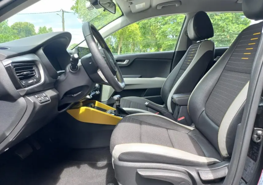 Vue intérieure côté conducteur du Kia Stonic noir 2025, avec sièges tissu noir et surpiqûres jaunes, console centrale jaune vif.