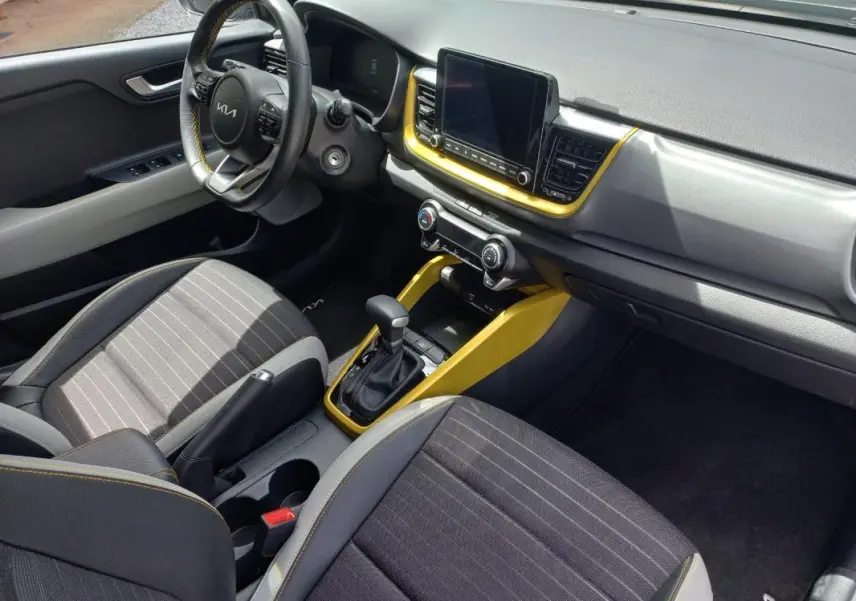 Vue intérieure côté conducteur du Kia Stonic 2025 noir, avec tableau de bord et console centrale soulignés de jaune vif.