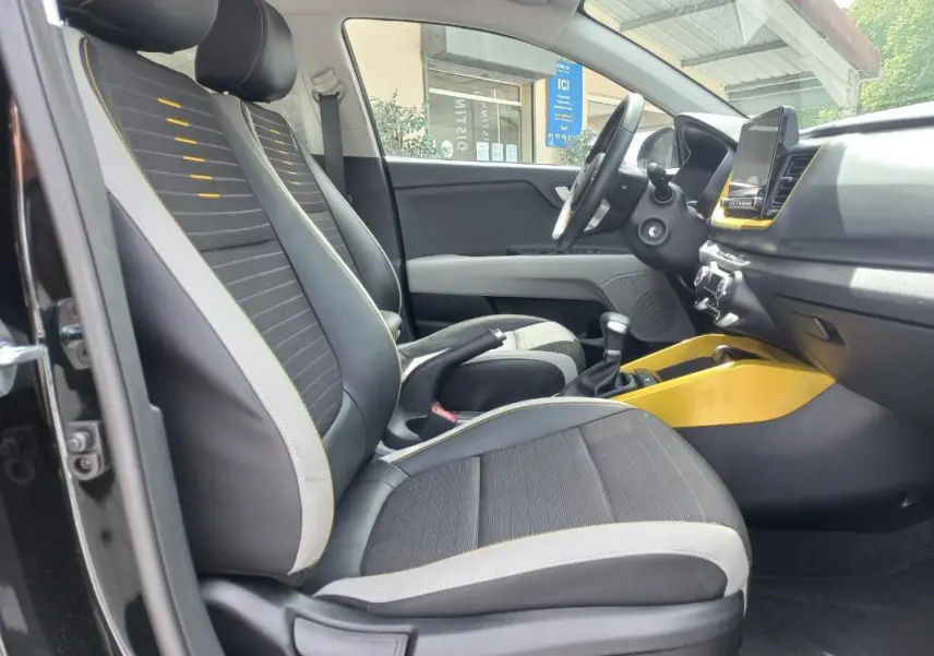 Vue intérieure côté conducteur du Kia Stonic noir 2025, avec sièges noirs et détails jaunes sur la console centrale.