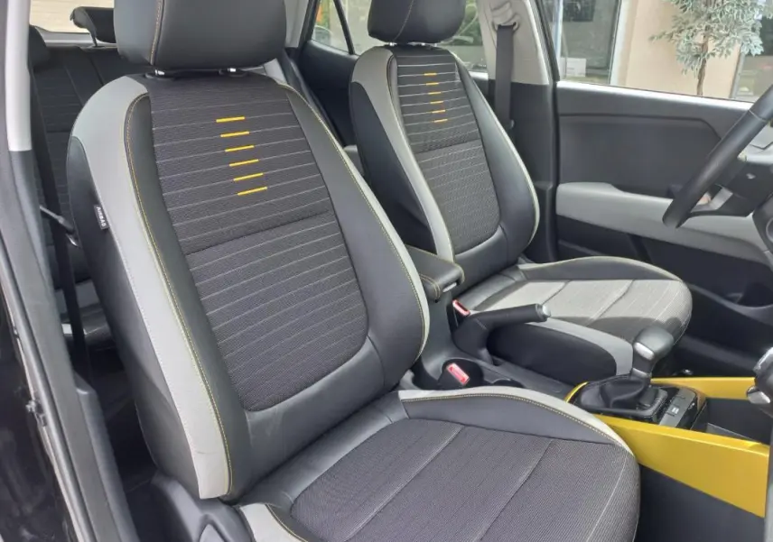 Vue intérieure des sièges avant du KIA Stonic 2025 noir, avec surpiqûres jaunes et console centrale jaune visible.