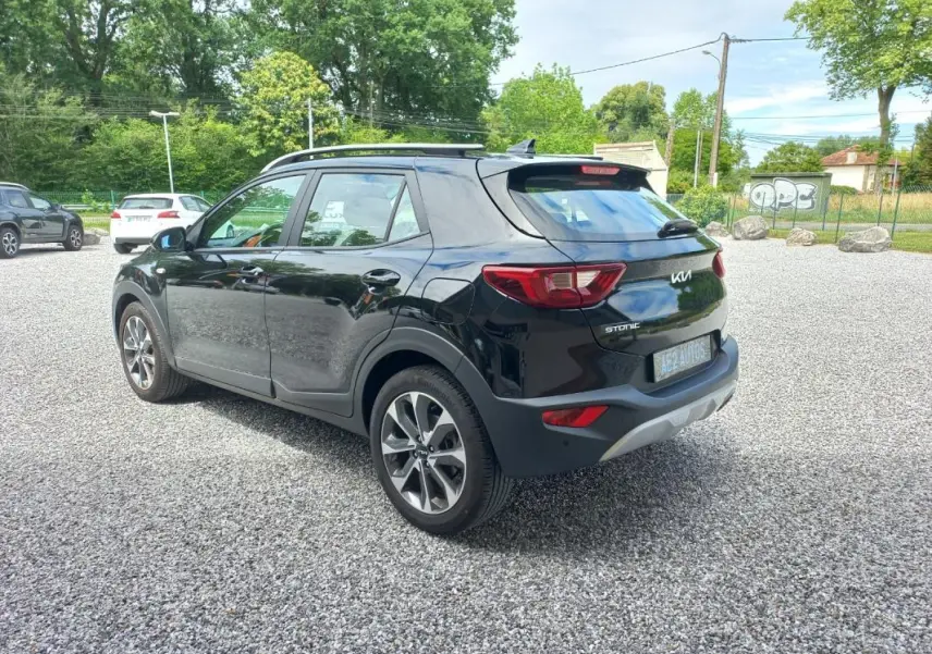 KIA Stonic noir vue 3/4 arrière droit, avec jantes alliage et toit avec barres de toit visibles.