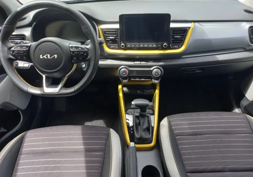 Vue intérieure avant du Kia Stonic 2025 noir, avec volant multifonction, écran central et contours jaunes autour de la console.