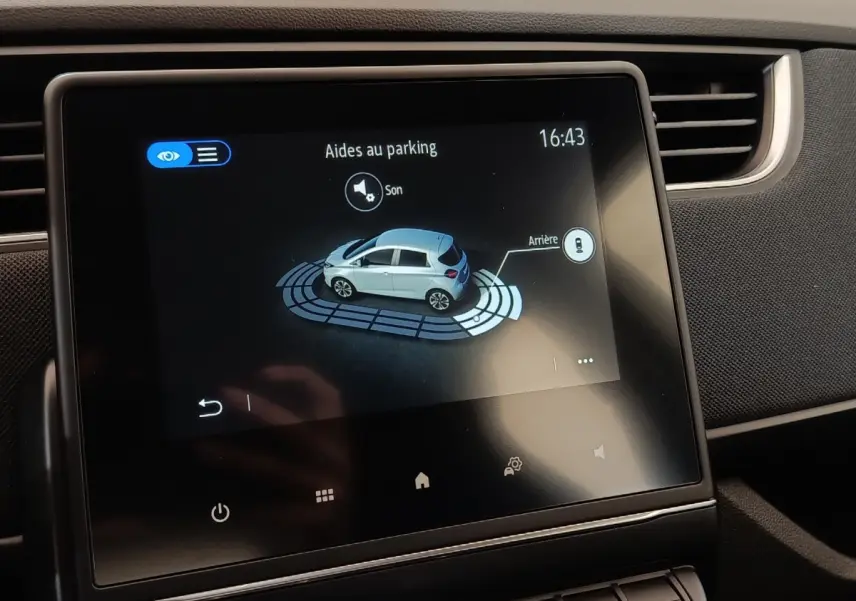 Écran tactile central affichant l’aide au parking d’une Renault ZOE blanche vue de profil côté gauche.