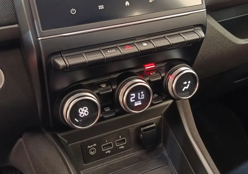 Gros plan sur la console centrale noire de la Renault ZOE blanche, avec commandes de climatisation numériques et ports USB visibles.