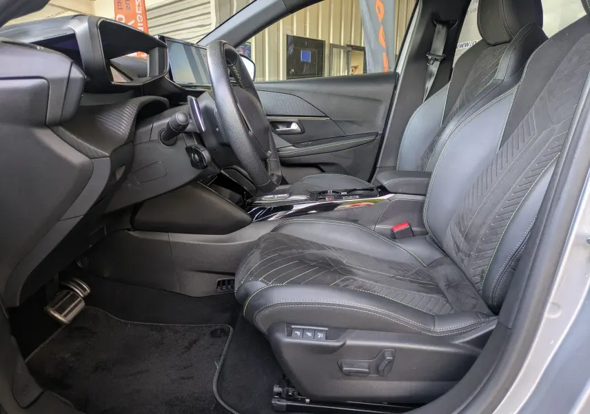 Vue intérieure côté conducteur de la Peugeot 208 HYBRID 145 GT 2025, sièges Alcantara noirs avec surpiqûres vertes.